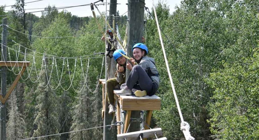 two outward bound students sit atop a platform during a ropes course exercise with outward bound